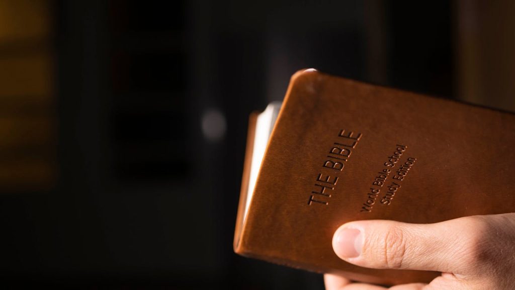 pexels-photo-9042043 Detailed view of a hand holding a leather-bound Bible indoors.